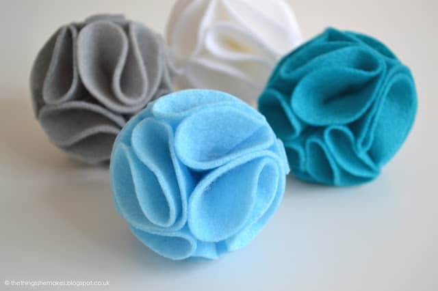 4 felt pom poms in blue, grey and white colors.