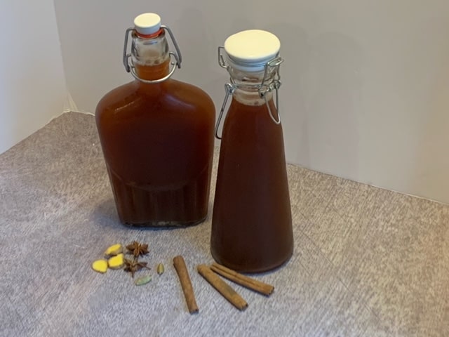 2 glass bottles of Chai Tea Concentrate sitting on a table with cinnamon sticks.