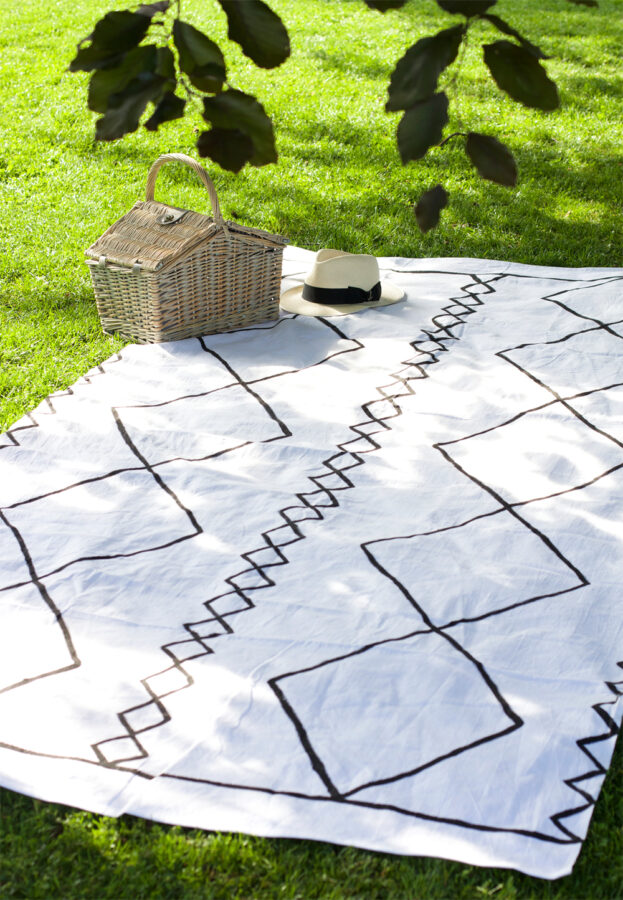 Black and white Moroccan print picnic blanket outside on the grass.