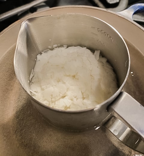 Soy candle wax flakes melted in a metal pitcher in a saucepan of water.