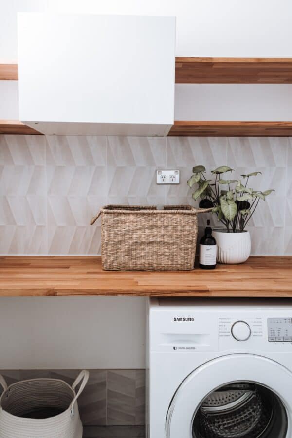 White washing machine with wooden shelf over the top.